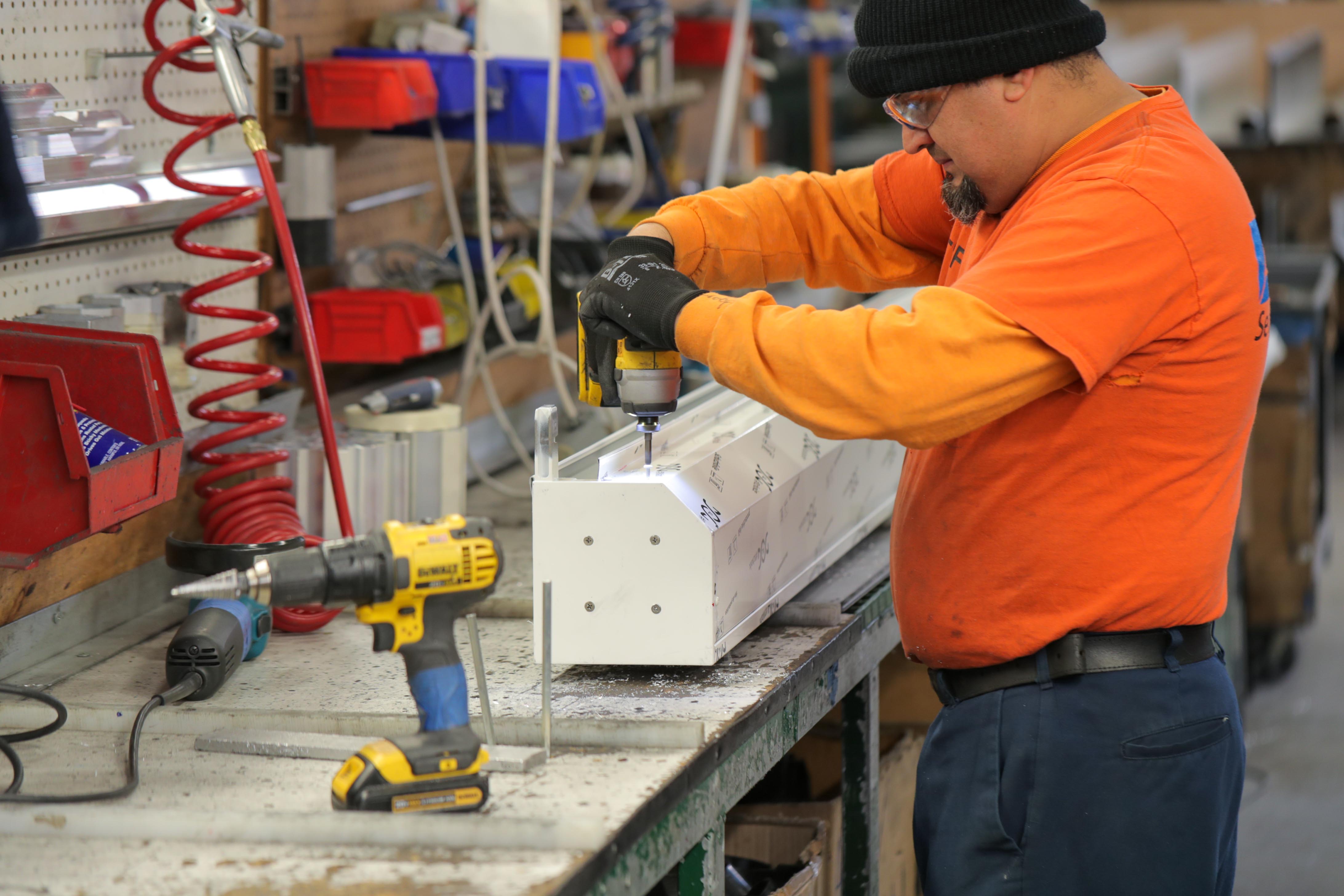 Image of a man engaged in manufacturing, using a drill to work on a piece of material.