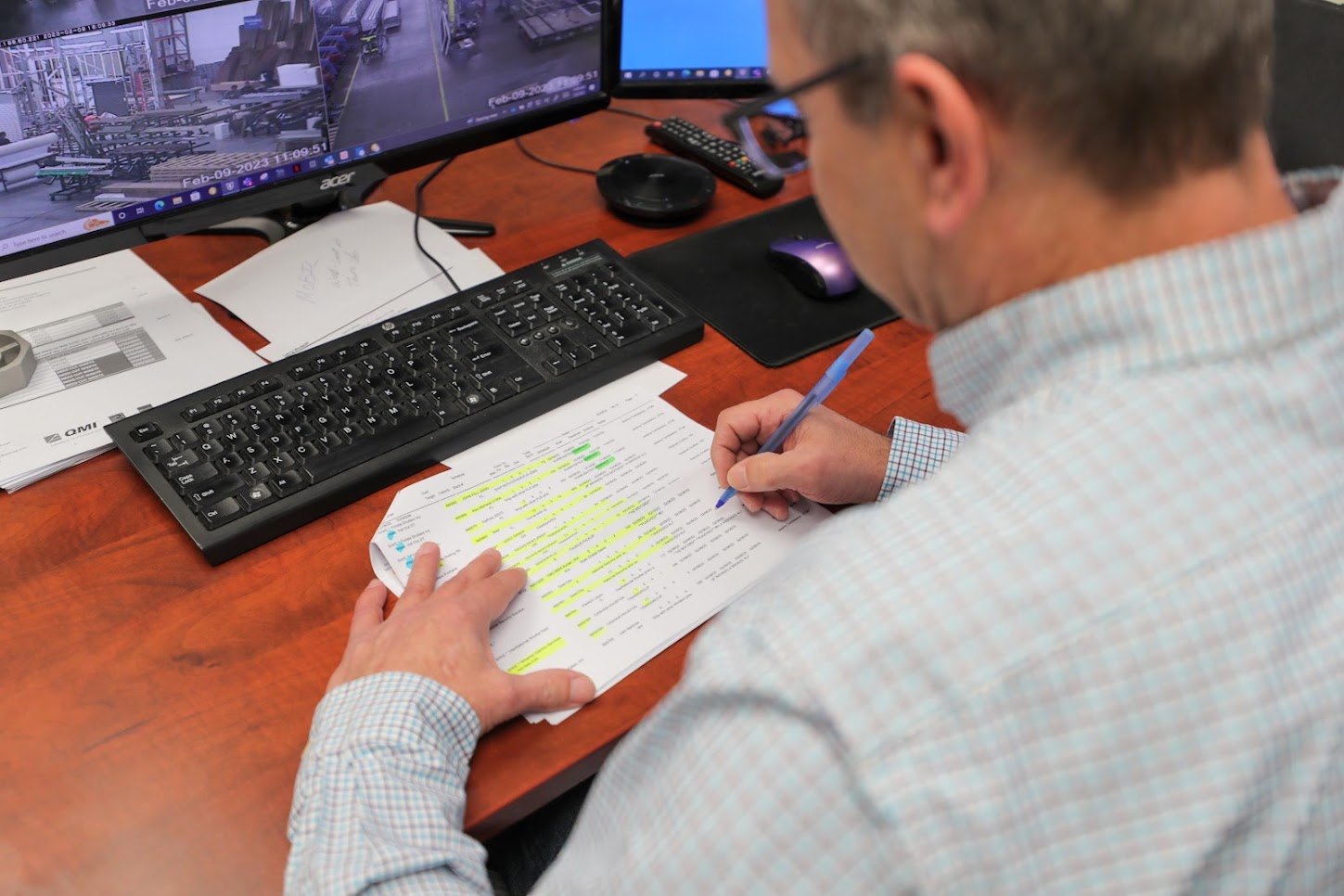 Focused man sitting at a desk, writing notes with a pen placed in front of a computer monitor and keyboard