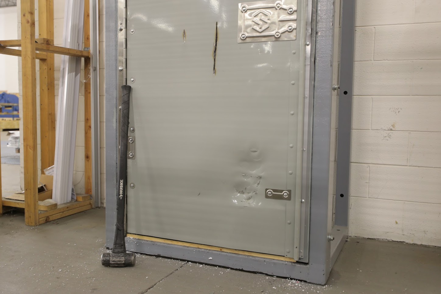 a sledge hammer rests below a high-security door after heavy impact testing